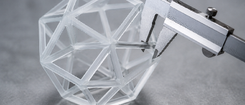 A precision tool measuring a complex translucent geometric structure on a minimalist background.