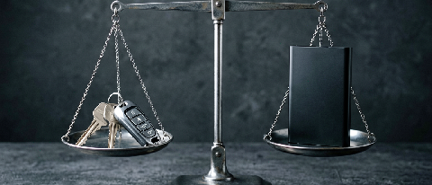 A symbolic representation of shifting responsibility in autonomous driving featuring a car key resting on a digital scale next to a data drive.