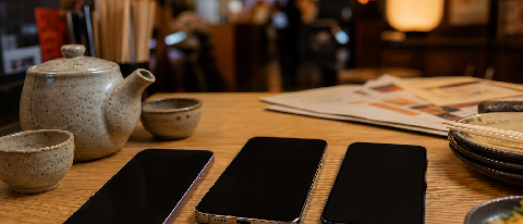 Three smartphones resting on a traditional Japanese izakaya table among menu sheets and tea