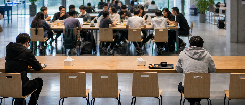 A half-empty cafeteria in a tech park, with one crowded table and one nearly deserted table, symbolizing the survival gap among AI agent startups.