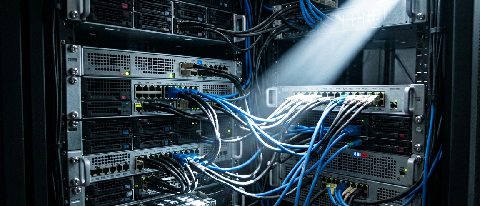 A complex server rack interior with tangled cables and a single focused light beam
