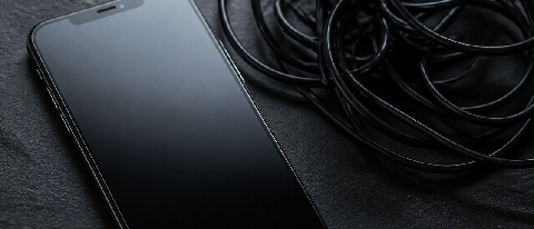 A minimalist editorial still life showing a sleek, modern smartphone resting on a dark surface, casting a shadow that subtly resembles a trap or cage, symbolizi