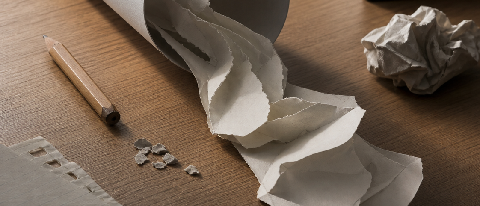 A paper cylinder being unraveled by a robotic hand on a desk with a grading rubric.