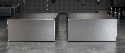 Two unlabeled, identical-looking metal boxes on a workbench, one with a measuring tape and a checklist, symbolizing the need to verify model specifications befo