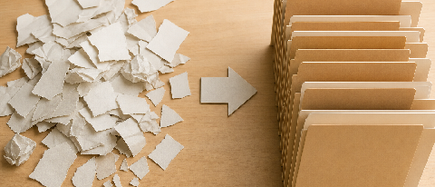 Editorial still life of scattered torn paper fragments next to neatly organized document folders on a desk