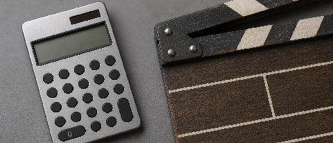 A minimalist editorial still life showing a calculator next to a film clapperboard on a clean desk, symbolizing the business side of video production.
