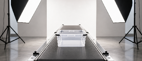 A clear plastic storage box on a minimalist studio conveyor belt lit by softbox lights, symbolizing automated e-commerce product videography.
