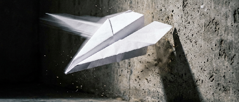 A white paper airplane mid-bounce against a textured wall