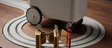 A small wheeled cart circling a miniature rail, stopped by three physical brake mechanisms: a blank gauge gate, a twin-token matching slot, and a red side-exit 