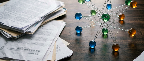 A still-life scene of stacked medical and financial documents with a small, illuminated knowledge-graph model on top, representing the shift from vector search 