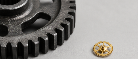 A giant industrial steel gear and a tiny precision watch gear side-by-side on a neutral background.