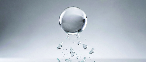 A surreal editorial still life showing a glass sphere shattering mid-air with fragments falling realistically against a blurred background, symbolizing physics 