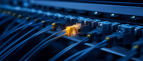 Macro shot of fiber optic cables in a data center with one point highlighted in amber light.