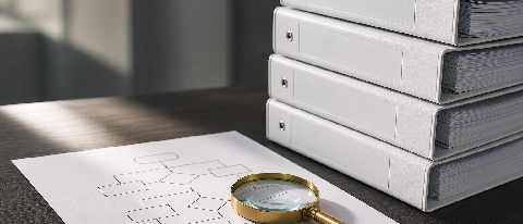 A clean, high-end editorial still life of organized compliance documents and a magnifying glass on a desk