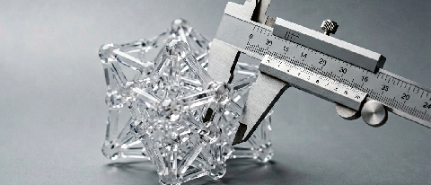 A translucent geometric lattice being measured by a precision metallic caliper on a neutral background.
