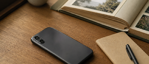 A smartphone resting on a wooden desk with a printed photo album and a notebook nearby, symbolizing on-device AI for photo search and input.