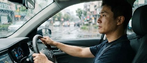 A driver's perspective inside a modern car during heavy rain, showing hands hovering near but not gripping the steering wheel, emphasizing trust in the automate